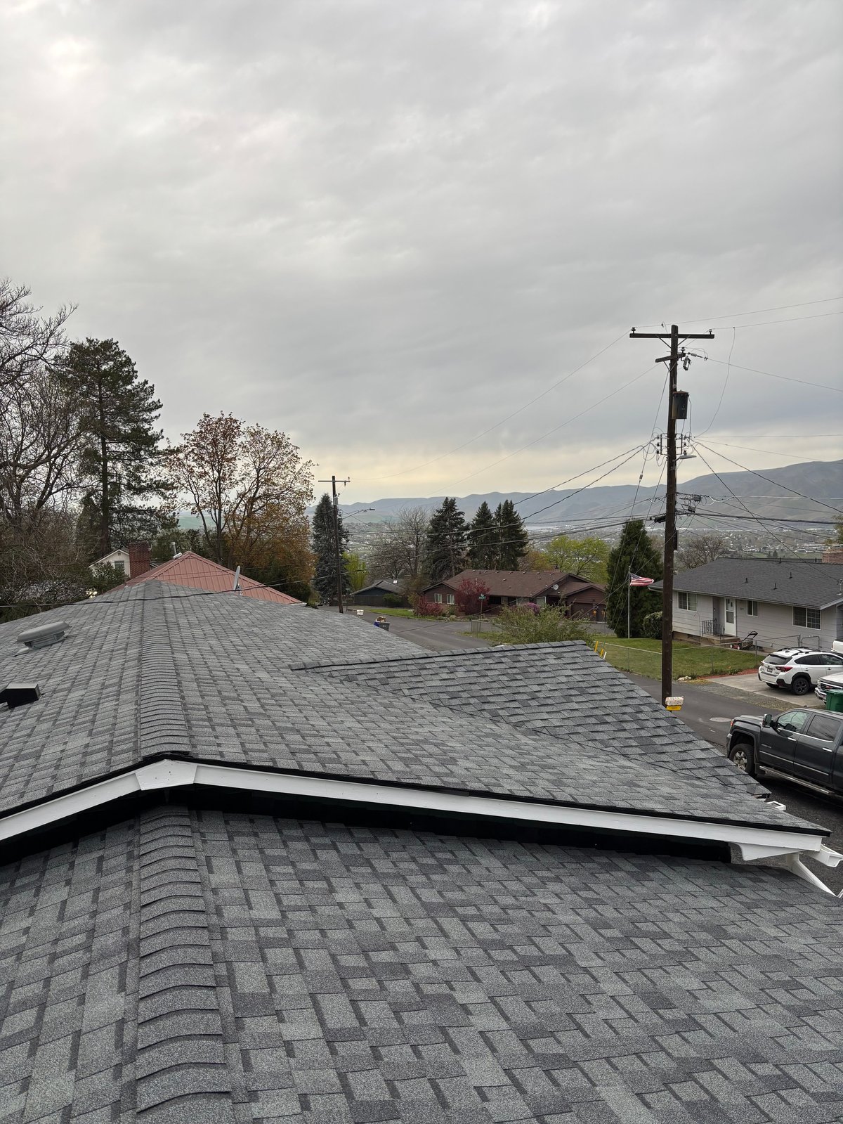 Aerial view of gray shingled roof with residential neighborhood and mountains under cloudy sky